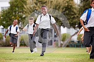 Excited Elementary School Pupils Wearing Uniform Running Across Field At Break Time