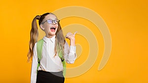 Excited Elementary Student Pointing Thumb At Copyspace Over Yellow Background