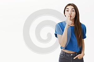 Excited energized woman asking keep secret safe not telling anoying posing with shush gesture against grey wall showing