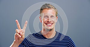Excited face, hand and man with peace sign in studio isolated on a grey background mockup space. Portrait, happy person