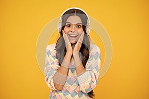Excited face. Teenager child girl in headphones listening music, wearing stylish casual outfit  over yellow