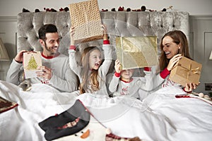 Excited Family In Bed At Home Opening Gifts On Christmas Day