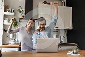 Excited young couple cheering for football team online at kitchen