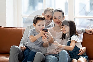 Excited family hugging, entertaining, using mobile phone.