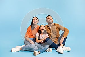 Excited family of parents and daughter looking up sitting, studio