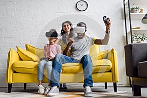 excited father and daughter playing video games while mother sitting behind