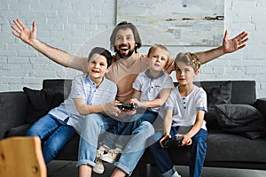 excited father and little sons sitting on sofa and playing video games together