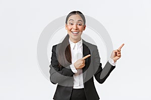 Excited female asian manager, saleswoman or real estate agent showing house for sale, pointing fingers right, trader