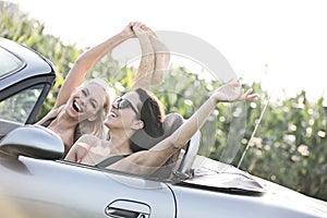 Excited female friends enjoying road trip in convertible on sunny day