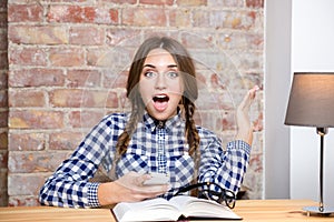 Excited female student sitting at the table with smartphone