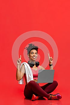 Excited fitness girl with laptop pointing up at copy space