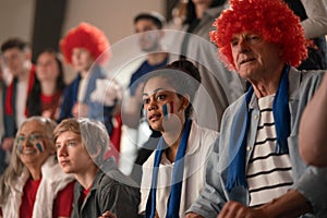 Excited football fans supproting French national team in live soccer match at stadium.