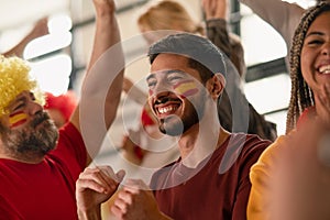 Excited football fans supproting spanish national team in live soccer match at stadium.