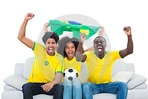 Excited football fans in yellow sitting on couch with brazil flag
