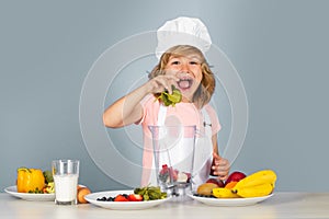 Excited funny chef cook. Child wearing cooker uniform and chef hat hold spinach preparing vegetables on kitchen, studio