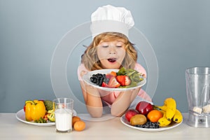 Excited funny chef cook hold plate with fruits. Kid boy in chef hat and apron cooking preparing meal. Little cook with