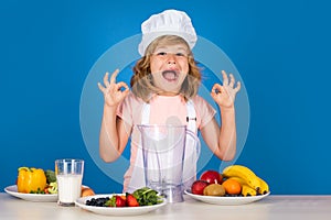 Excited funny chef cook. Kid boy in chef hat and apron cooking preparing meal. Little cook with vegetables at kitchen