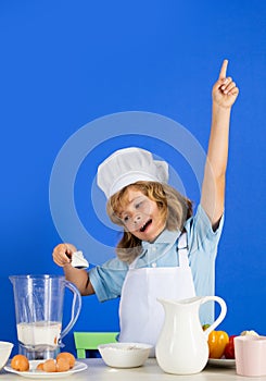 Excited funny chef cook. Portrait of a 7, 8 years old child in cook cap and apron cooking food with flour in kitchen