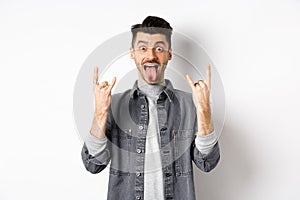 Excited funny guy showing tongue and heavy metal horns sign, enjoying party or event, having fun, standing on white