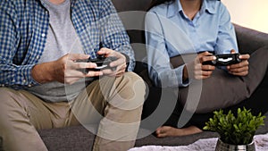 Excited funny young couple playing video games holding game controller sitting on sofa having fun with new technology console