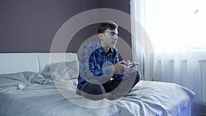 Excited gamer boy sitting on couch, playing video games on console. Man plays with wireless controller. Male holding joystick on h