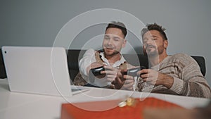 Excited gay couple playing video games on laptop using joystic