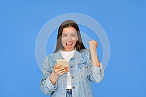 Excited gen z Latin girl celebrating win using mobile cell phone on background.