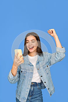 Excited gen z Latin girl celebrating win using mobile cell phone on background.