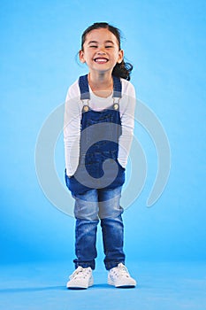 Excited girl child, fashion and studio portrait with jeans, dungaree and trendy style by blue background. Female kid