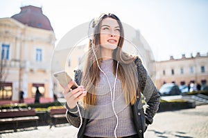 Excited girl dancing and listening music with headphones and smart phone in the street