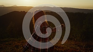 Excited girl dancing in mountains at sunset. Woman turning around in meadow