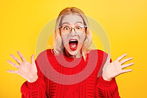 Excited girl dressed in red casual and glasses opened mouth in surprise and bulged eyes against yellow background, isolated. Portr