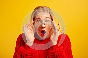 Excited girl dressed in red casual and glasses opened mouth in surprise and bulged eyes against yellow background, isolated. Portr