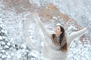 Excited girl enjoying snow in winter raising arms