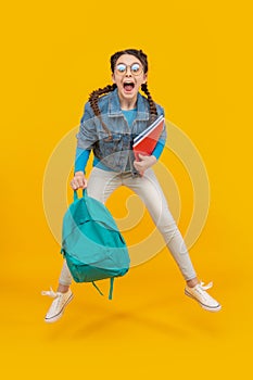 Excited girl jumping after school yellow background. Energetic teenager screaming in midair, school