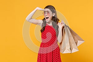 Excited girl in red summer dress, eyeglasses isolated on yellow background. People lifestyle concept. Hold package bag