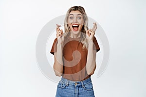 Excited girl screams with crossed fingers, making wish, hoping to win something, standing happy against white background