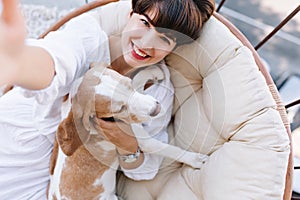 Excited girl with short brown hair laughing while taking photo of herself with beagle dog. Portrait from above of happy