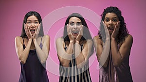 Excited girls looking on camera, surprised by huge discounts, pink background