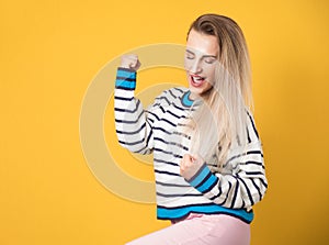 Excited gorgeous young woman with closed eyes and clenched fists, isolated on yellow background. Yes concept. Good news