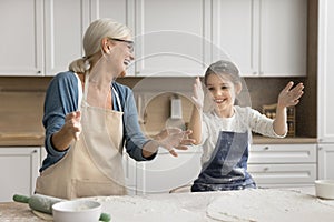 Excited grandmother and happy granddaughter girl in aprons throwing flour