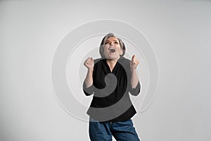 Excited grey haired woman shouting loud in amazement. Pretty mid aged grey haired woman in black shirt isolated on grey