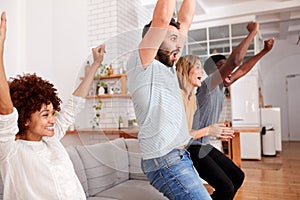 Excited Group Of Friends Sitting On Sofa Watching Sports On TV And Celebrating