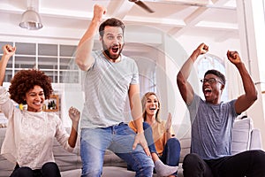 Excited Group Of Friends Sitting On Sofa Watching Sports On TV And Celebrating