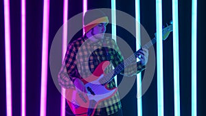 An excited guitarist plays an electric guitar in the studio surrounded by pink and blue neon tubes. A contented person