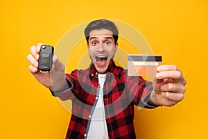 Excited Guy Showing Car Key And Credit Card, Yellow Background