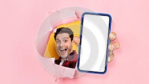 Excited guy showing white empty smartphone screen through torn paper