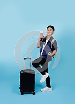Excited handsome Asian male tourist wearing casual clothes holding passport ticket standing isolated on light blue background. air