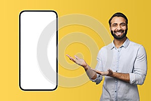Excited handsome hispanic bearded man points palms at huge smartphone with empty blank screen