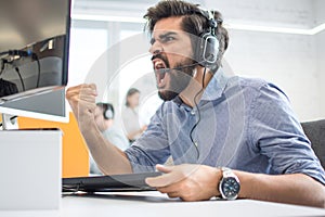 Excited handsome male customer support operator with headset celebrating success while working in call centre.